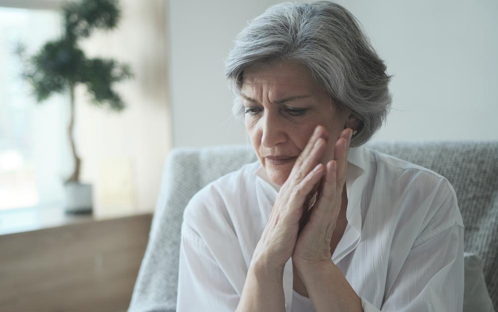 Elderly senior woman massaging her temples to reduce her headache. Older lady feeling scared, anxious, and thinking of sickness or mental health while suffering from a severe migraine or memory loss.